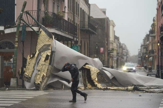 Slide 1 of 11: A man passes by a section of roof that was blown off of a building in the French Quarter by Hurricane Ida winds, Sunday, Aug. 29, 2021, in New Orleans.
