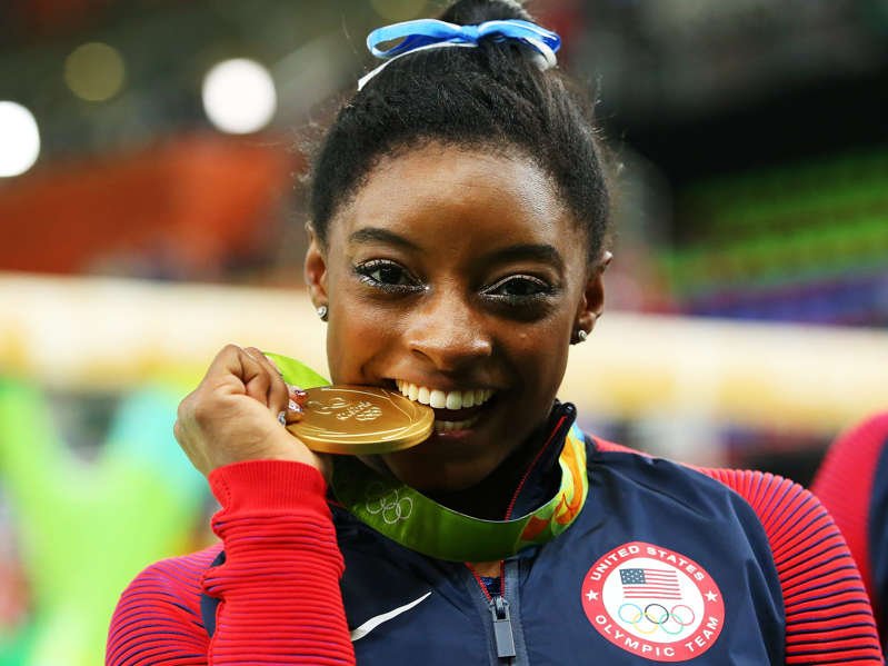 a close up of Simone Biles eating a donut: Biles poses with her gold medal after the Individual All-Around final at the Rio Olympics in 2016. Alex Livesey/Getty Images