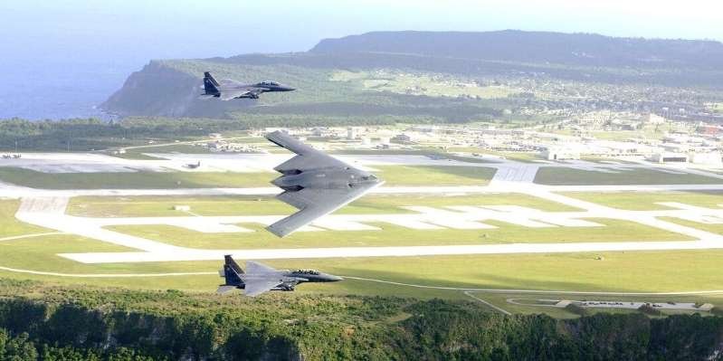 a fighter jet sitting on top of a mountain: F-15E Strike Eagles and a B-2 Spirit bomber fly in formation over Andersen Air Force Base on Guam US Air Force