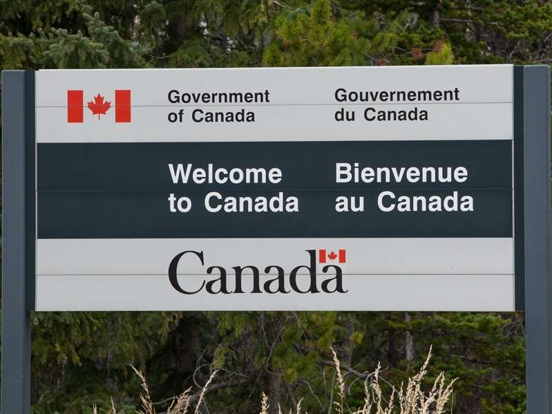 a sign on the side of a tree: A "Welcome to Canada" sign at the US-Canada border. Shutterstock.com
