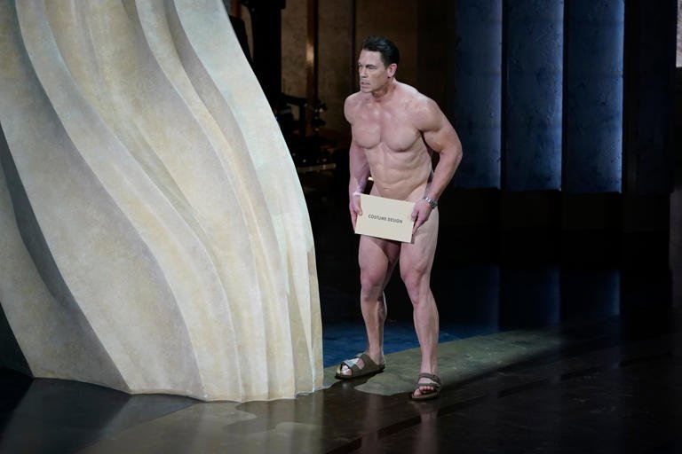 A naked John Cena (with a strategically placed envelope) presents the award for achievement in costume design during the 96th Oscars.