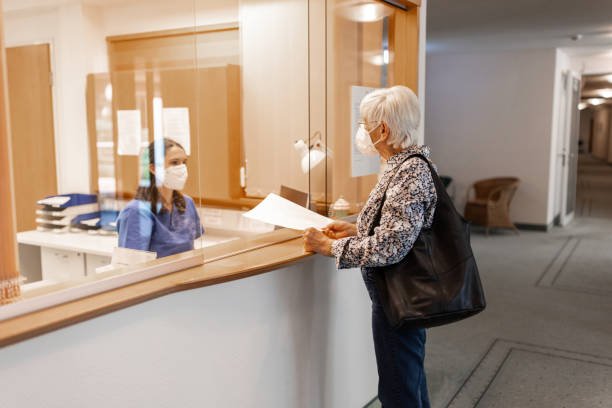 nurse assisting a senior patient at the hospital reception desk - covid 19 hospital reception stock pictures, royalty-free photos & images