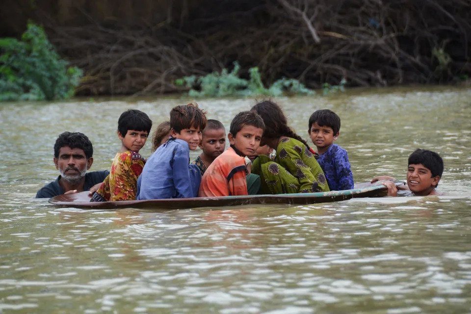 People push a satellite dish filled with children across a flooded area.