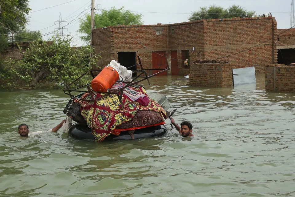 Residents, with only their heads showing above water in a flooded area, pull a raft piled with their belongings.